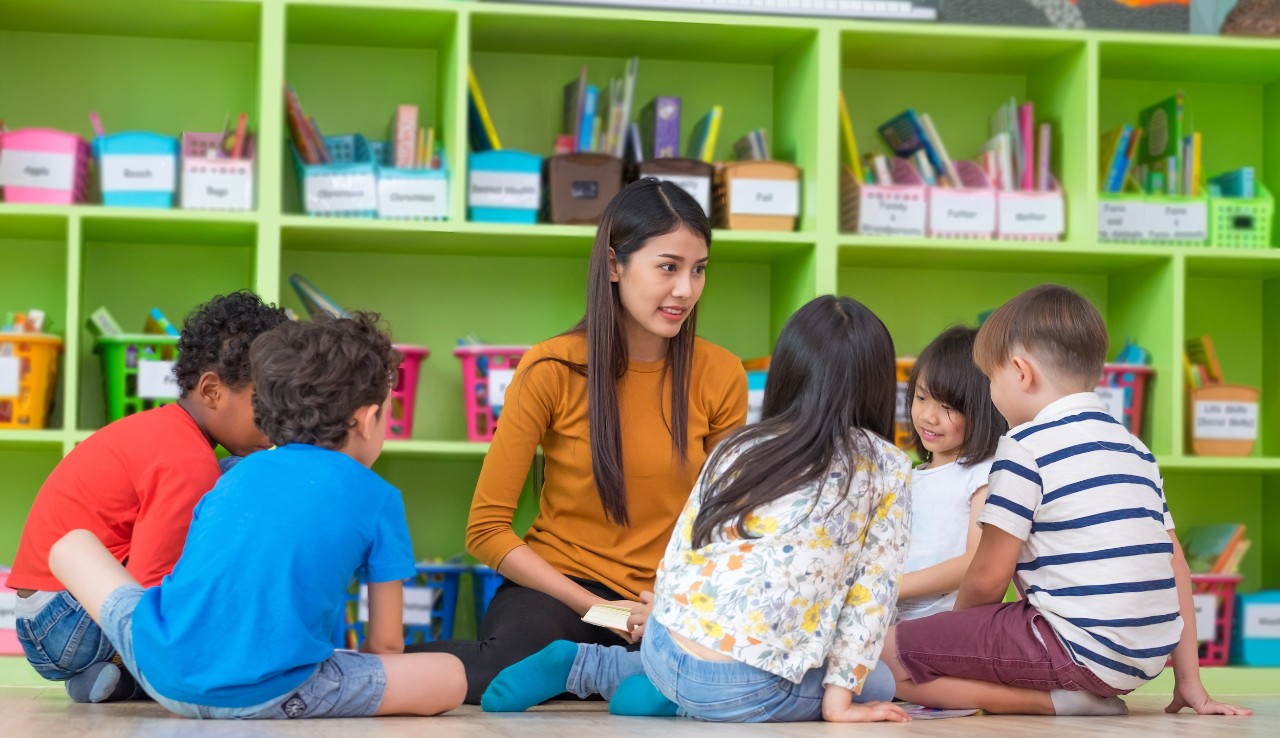 Asian female teacher teaching mixed race diversity group of kids reading book sitting on library floor in classroom,Kindergarten pre school concept. Asian female teacher teaching mixed race diversity group of kids reading book sitting on library floor in classroom,Kindergarten pre school concept