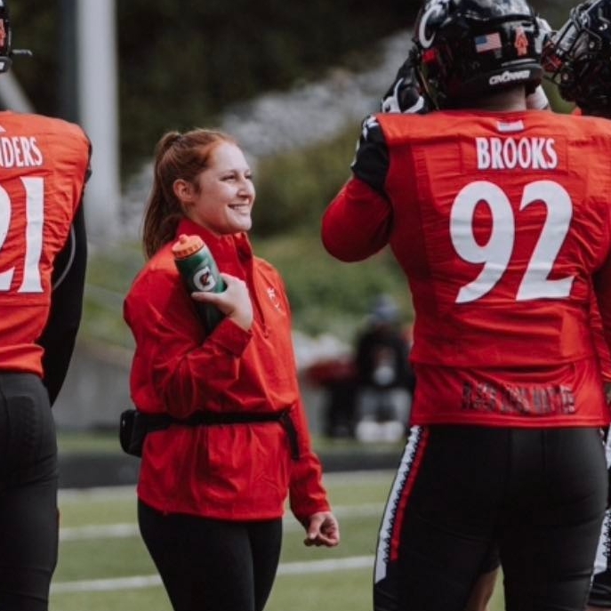 Bryn Cortez, 3rd year  in the Health Science - Pre Athletic Training Program, holds water on the football field.