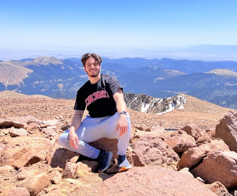Brenden Benjamin, Second-year DTP student sits on top of a mountain.